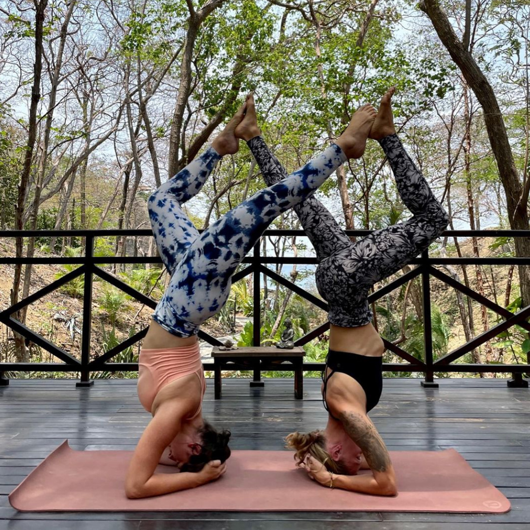 Cala Azul Yoga pose with two women in a shared position standing on head with feet touching