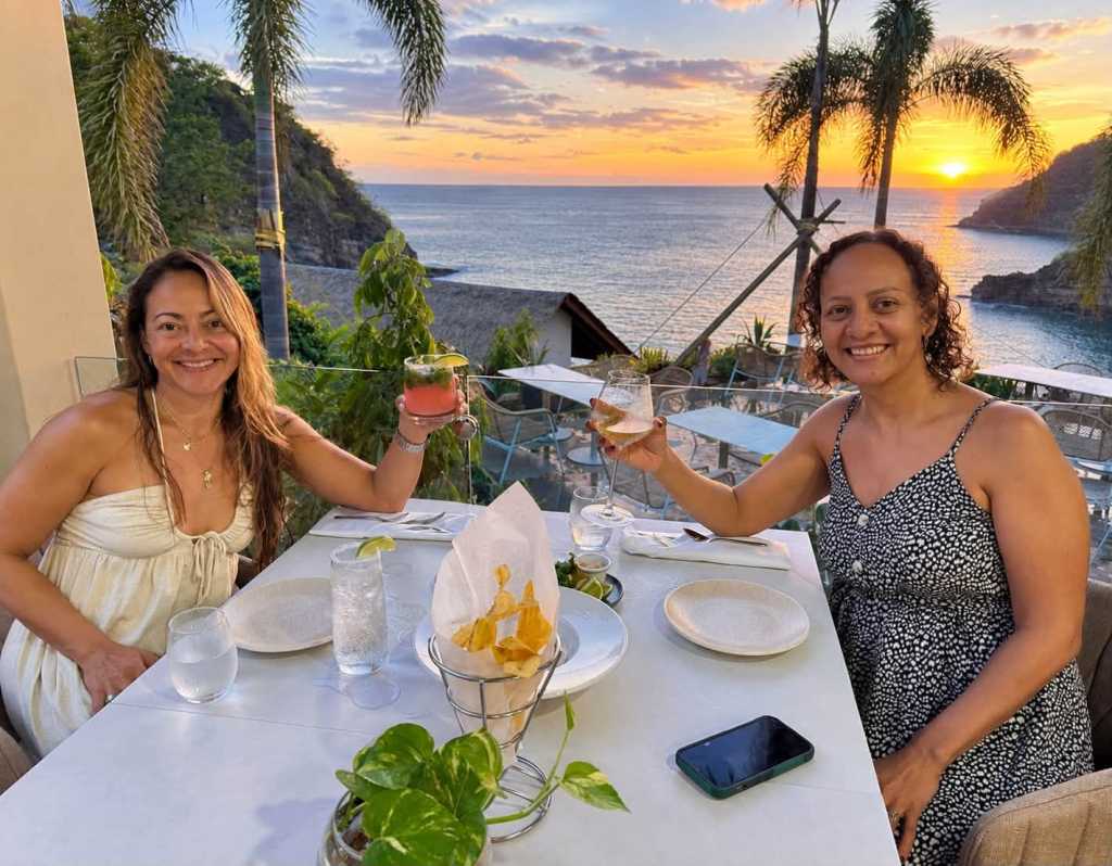 Two guests enjoying dinner and drinks overlooking the Pacific Ocean at sunset
