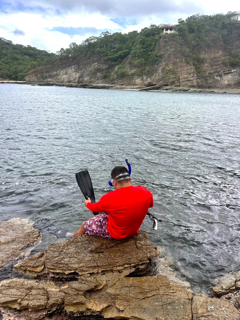 Guest sitting on coastal rocks overlooking a quiet Pacific bay