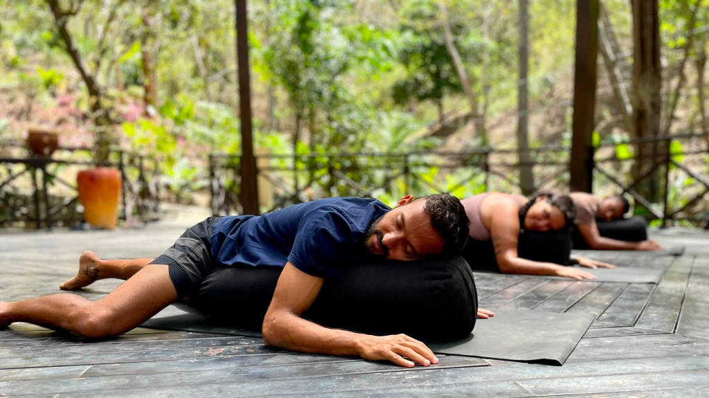 Guests practicing restorative yoga on an outdoor wooden pavilion at Bliss Resort